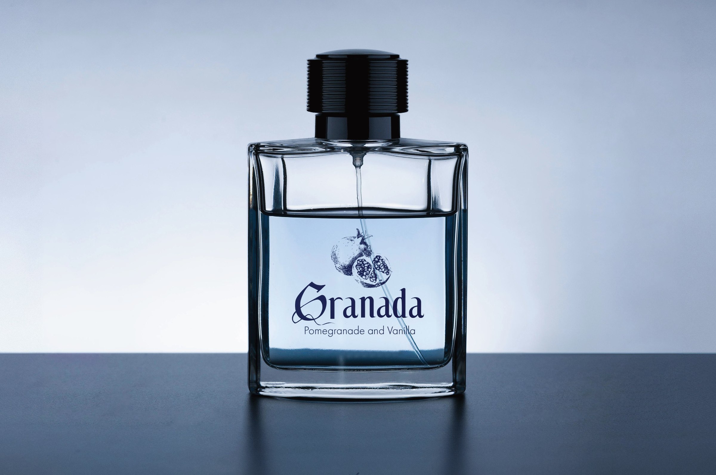 A square perfume bottle with a pomegranate drawing and the word Granada in the typeface, above the line Pomegranade and Vanilla.