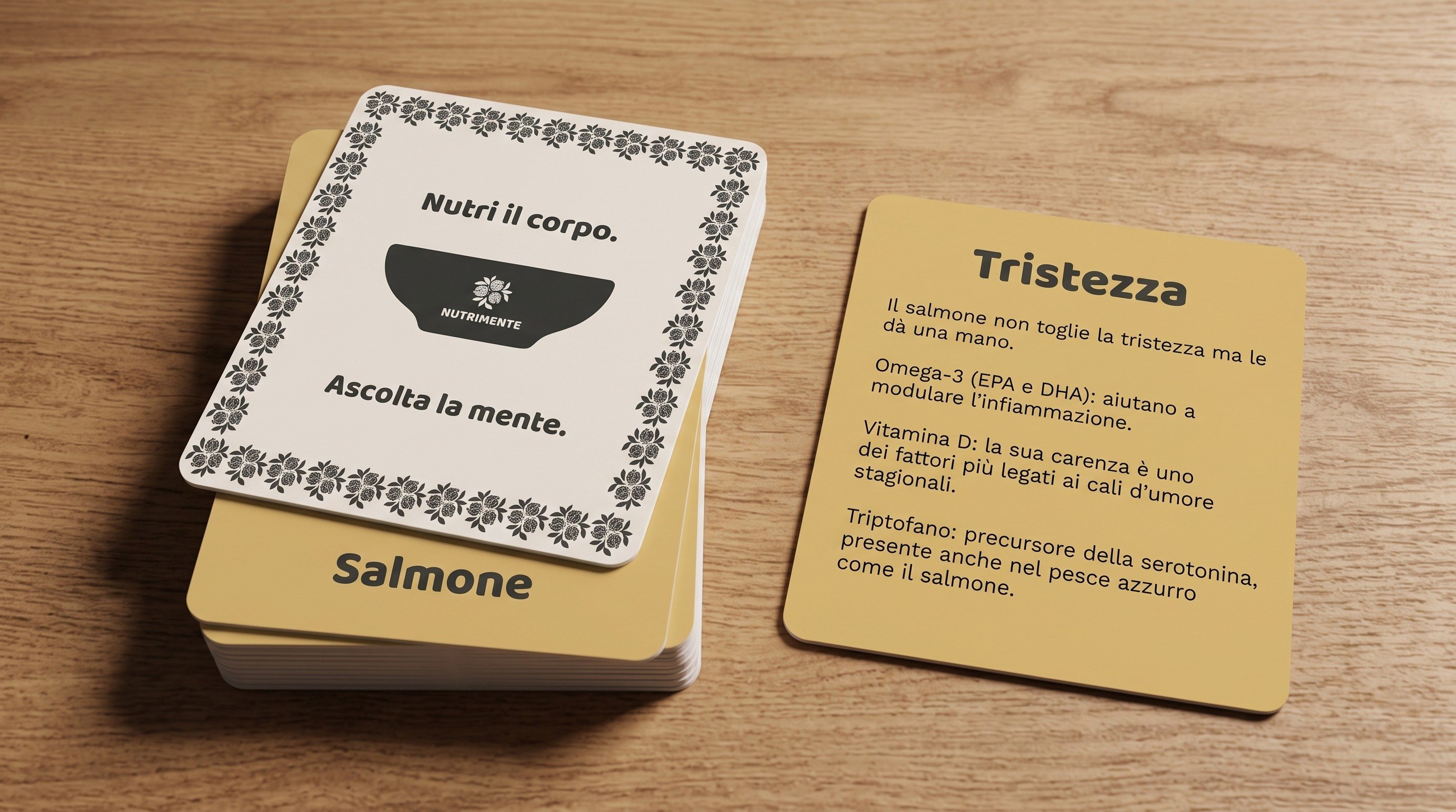 Memory game cards on a wooden table: the back with the logo and the payoff, and the sadness card about salmon.