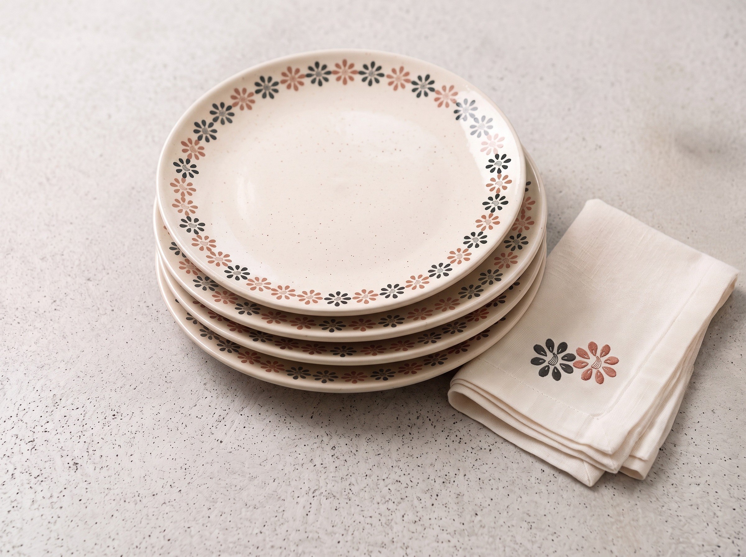 A stack of ceramic plates with the pomegranate flower pattern on the rim and a matching linen napkin.
